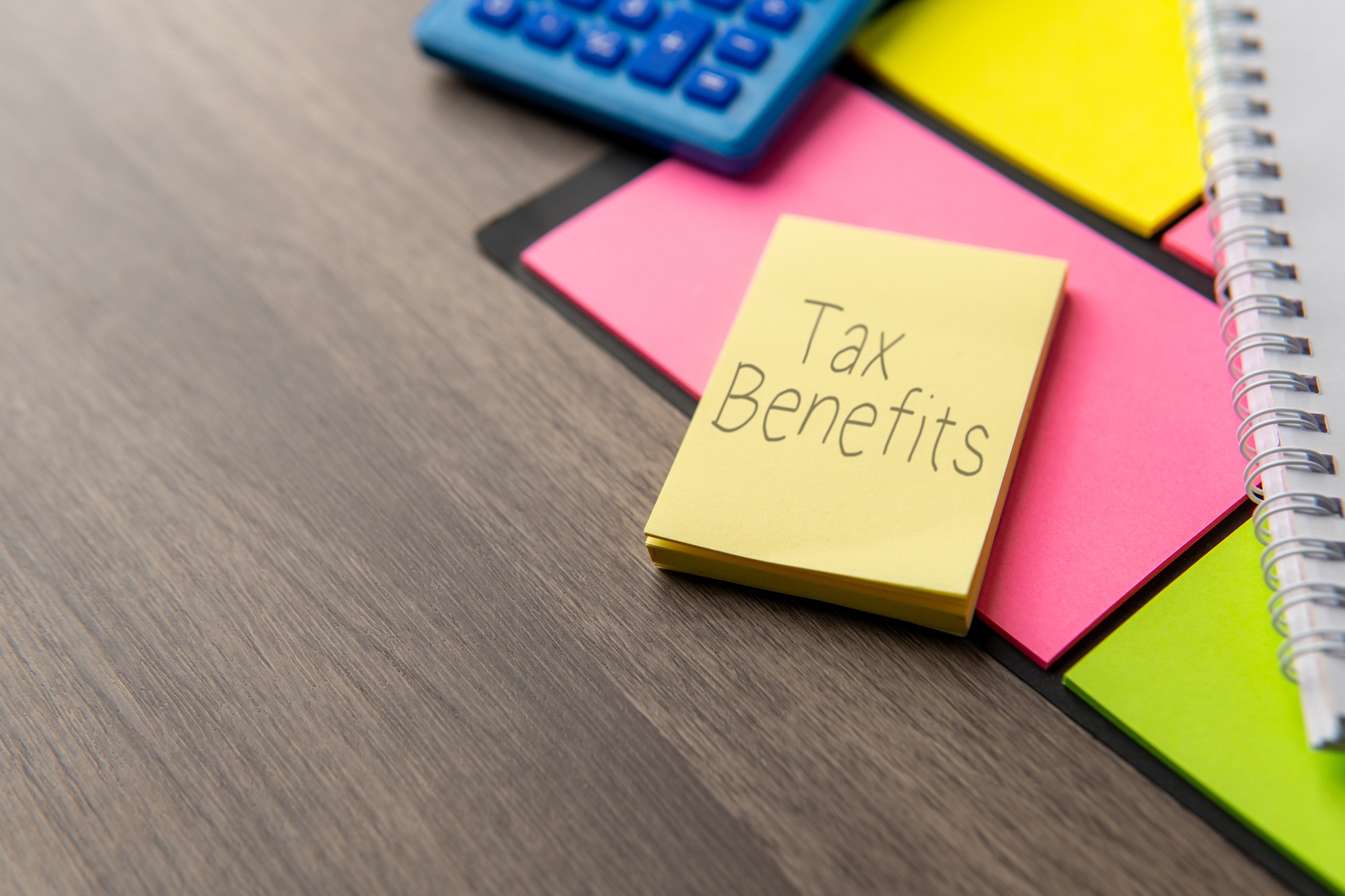 A yellow sticky note with the words "TAX BENEFITS" alongside a blue calculator.